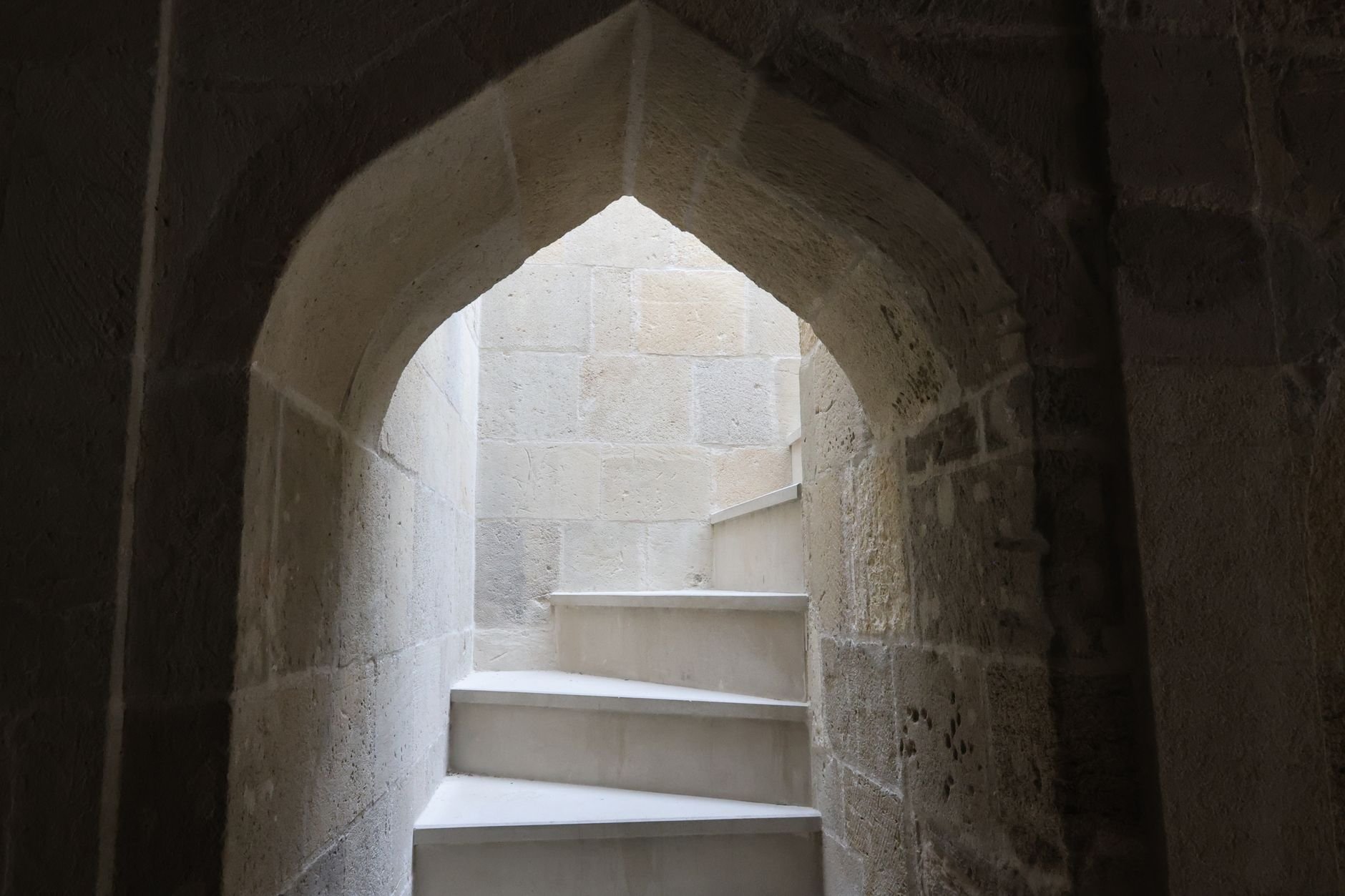 Ancient stone archway leading to a spiral staircase in dim light.